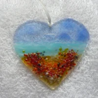 Fused glass coastal heart suncatcher with flowers on the beach, hanging from a white ribbon.