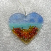 Fused glass heart suncatcher. Background in blue, turquoise and tan, with frit in colours of red, orange and yellow. Hanging from a white ribbon.
