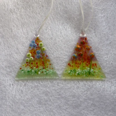 Two triangular shaped glass suncatchers, one with blue and green hearts, the other with multicoloured beads for flowers with green stems. This is a very tactile design hanging from white ribbon.