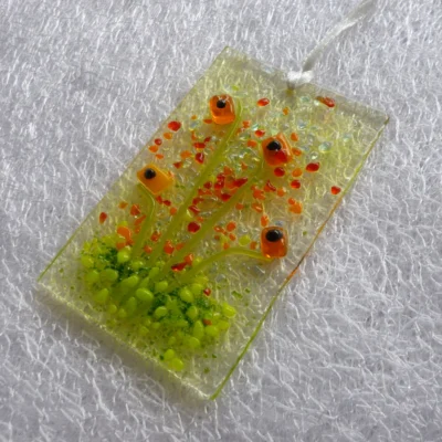 Side view of orange flower suncatcher, showing very tactile flowers, stems and detail. Hanging from a white ribbon.