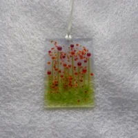 Tactile bead flowers fused on to a glass suncatcher with orange frit for decoration. Hangs from a white ribbon.