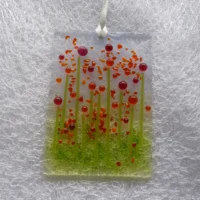 Rectangle shaped glass suncatcher with red and orange quirky bead flowers with green stems. Orange frit for decoration and hangs from a white ribbon.
