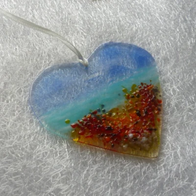 Heart suncatcher from a different angle with seaside view, hanging from a white ribbon.