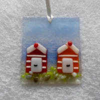 Red and orange striped beach huts create a coastal suncatcher, hanging from a white ribbon. This is a very tactile design with large frit to create stones.