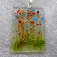 Rectangle shaped fused glass suncatcher with multicolour transparent beads to resemble quirky flowers with green glass stringers for stems. Hole at the top with a white ribbon threaded through to hang from.