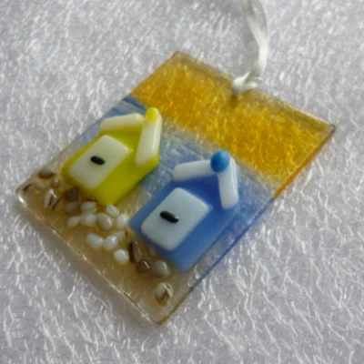 Side view of coastal suncatcher with yellow and blue beach huts trimmed with white, large glass (crushed glass) frit for stones and hangs from a white ribbon.