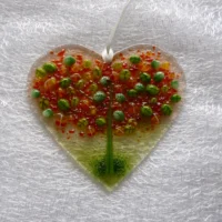 Heart suncatcher in glass with autumn inspired tree fused on top in green, red and orange hanging from a white ribbon.