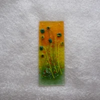Fused glass suncatcher with quirky square flowers in light and dark green with black centres and long stems. Green and red frit adds decoration. Hangs from a clear cord.