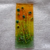 Long fused glass suncatcher with quirky green flowers and a background of green, orange and yellow hanging from a clear cord.