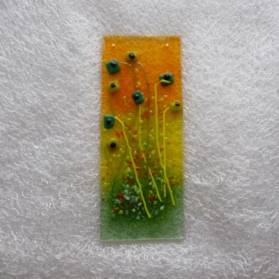 Fused glass suncatcher with a background of red yellow and green. Light and dark green quirky square flowers with black centres and long stems. Hangs from a clear cord.