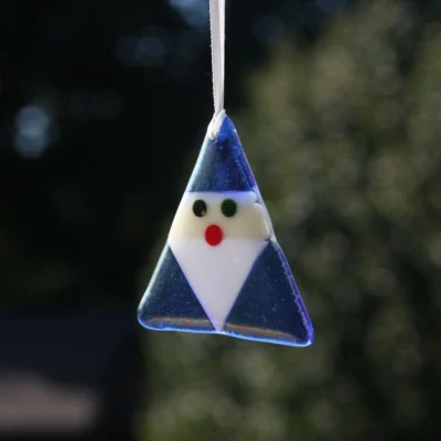 Triangle shaped blue fused glass Santa with white beard and red nose, hanging from a white ribbon.