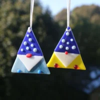 Two fused glass gonks, one has a light blue body and dark blue hat with glass beads. The other has a yellow body with dark blue hat and glass beads. Glass beads used for detail in nose and feet.