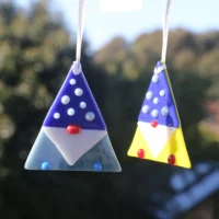 Two fused glass gonks, one in blue and the other yellow hanging from white ribbons.
