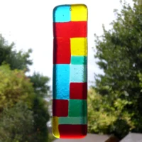 Vibrant fused glass suncatcher with blocks of colour (different shapes) in transparent red, yellow, blue and green hanging from a clear cord.