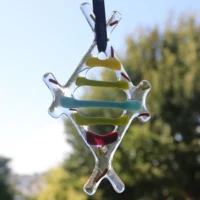 Diamond shaped fused glass suncatcher hanging from a black ribbon. Strips of yellow, green, turquoise and red laying across the suncatcher.