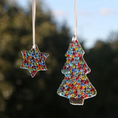 Multi-colour fused glass Christmas tree and star hanging from a white ribbon. Colours of red, yellow, blue, orange, yellow, green glass beads on top of a clear glass.