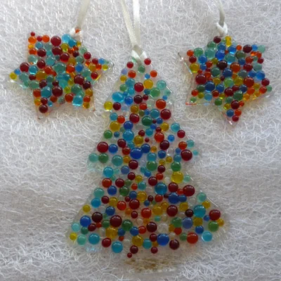 Christmas tree and two colourful stars hanging from a white ribbon laying on a white cloth.