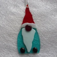 Tactile fused glass gonk in red, turquoise and white, with a big red nose and red shoes, hanging from a white ribbon.