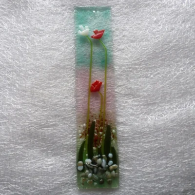 Long fused glass flower suncatcher in red and white, laying on a white cloth.