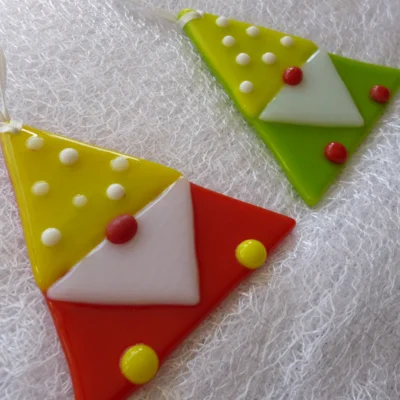 Red and green fused glass gonks laying on a white cloth, with red, white and yellow detail.