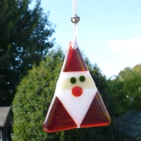 Red iridised glass Santa in a triangle shape hanging from a white ribbon. Body and hat is red, beard white.