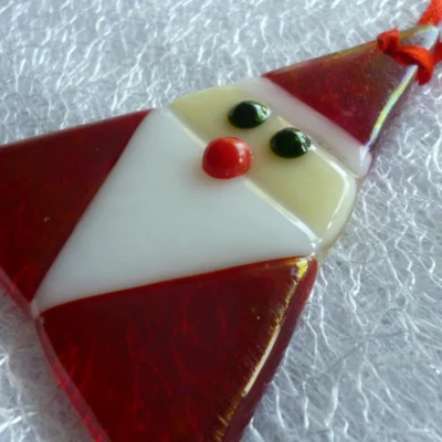 Side view of glass Santa Claus with a slight shimmer from the irid glass, hanging from a red ribbon.