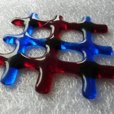 Close up of small red and blue fused glass lattice suncatcher laying on a white cloth.