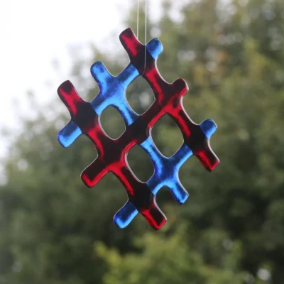 Red and blue lattice fused glass suncatcher hanging in a window. Red and blue glass has a slight sheen to it and hanging from a clear cord. Design is a lattice pattern with four holes in the middle.