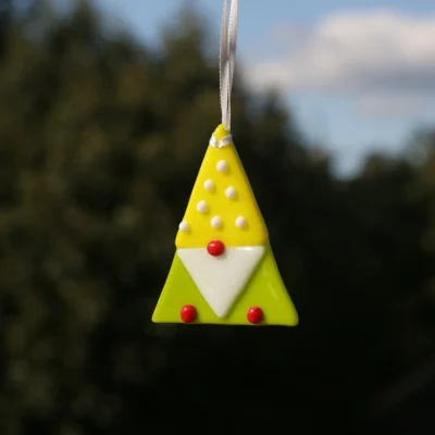 Triangle shaped fused glass gonk in yellow and green, white beard, red nose and feet, white beads on yellow hat. Hanging from a white ribbon