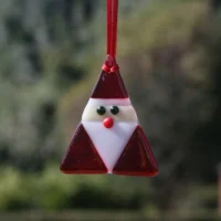Iridised fused glass triangle shaped Santa hanging from a red ribbon.