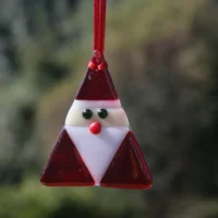 Triangle shaped fused glass Santa Claus, with glass beads for nose and eyes, hanging from a red ribbon.