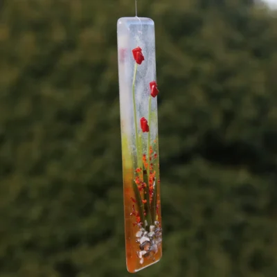 Side view of long red flower suncatcher, with white, yellow and red background and tactile flowers, stems and leaves.