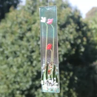 Long and slim fused glass flower suncatcher. Tactile red and white flowers, along with green glass leaves. Hanging from a clear cord.