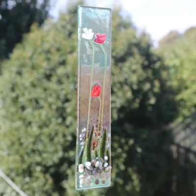 Fused glass red and white flower suncatcher hanging from a clear cord.