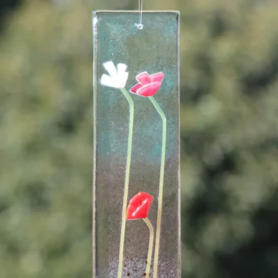 Close up of white and red flowers on a glass back, green spaghetti like glass for stems, hanging from a clear cord
