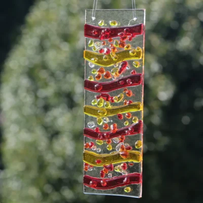Suncatcher hanging in sunlight with Red and Orange stripes, with yellow frit decoration.