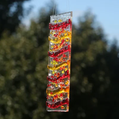 Different view of red, yellow, orange, glass wave suncatcher hanging in a window.