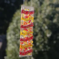 Colourful red, yellow and orange fused glass suncatcher at an angle hanging outside.