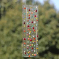 Fused glass suncatcher with thin spaghetti like glass and colourful beads fused on to a clear glass. Beads in colours in red, orange, blue, yellow and green, hanging from a clear cord.