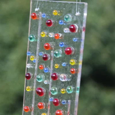 Close up of glass beads and strings on clear glass suncatcher. Beads in colours of green, blue, red, yellow, orange and clear.