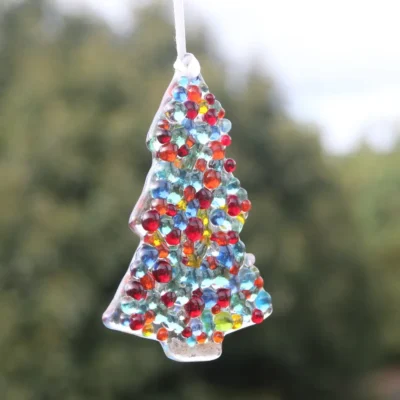 Side view of fused glass Christmas tree suncatchers with glass beads on top hanging from a white ribbon. Glass beads in colours of red, green, yellow, orange, blue and turquoise.