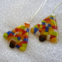Two fused glass Christmas tree decorations laying at an angle on a white cloth, ribbon attached to hang from