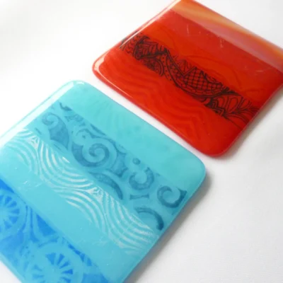 Two fused glass coaster set in red and blue, made up of different glass strips for a unique design.