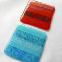 Red and Blue fused glass coaster set laying at an angle.