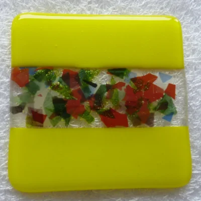 Vibrant yellow handmade fused glass coaster with decorative centre strip made with colourful confetti glass in red, green, white and blue.