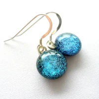 Blue dichroic glass earrings laying at an angle with sterling silver ear wires attached