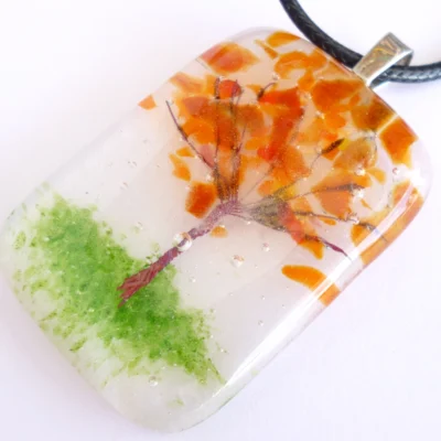 Close up of handmade Autumn Tree Fused Glass Pendant Necklace with orange frit and copper wire