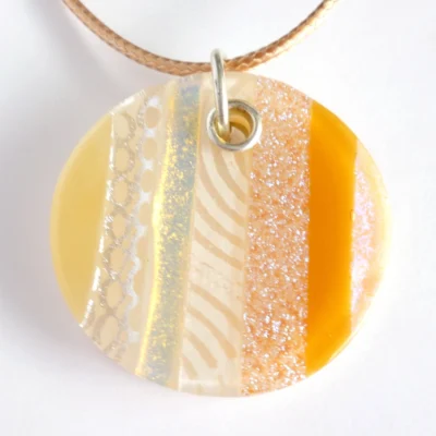 Close up of handmade round beige dichroic fused glass pendant with sterling silver fitting