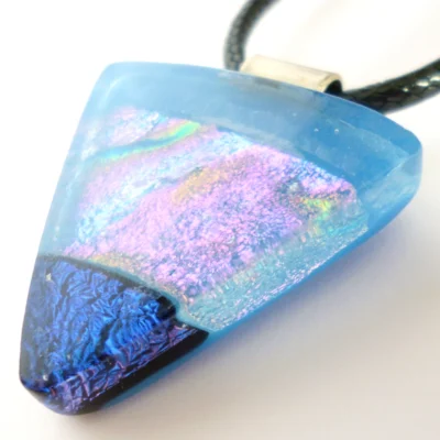 Close up of handmade blue dichroic fused glass pendant showing turquoise pink and gold shimmer with sterling silver bail