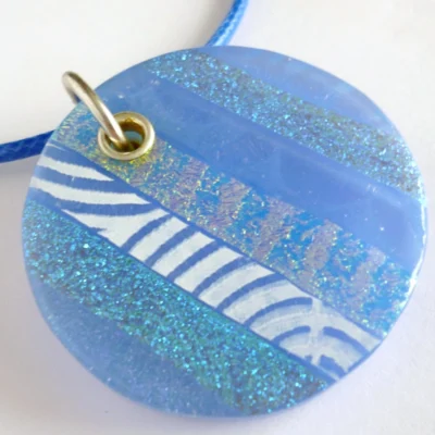 Close up of handmade blue dichroic fused glass pendant with sterling silver fitting